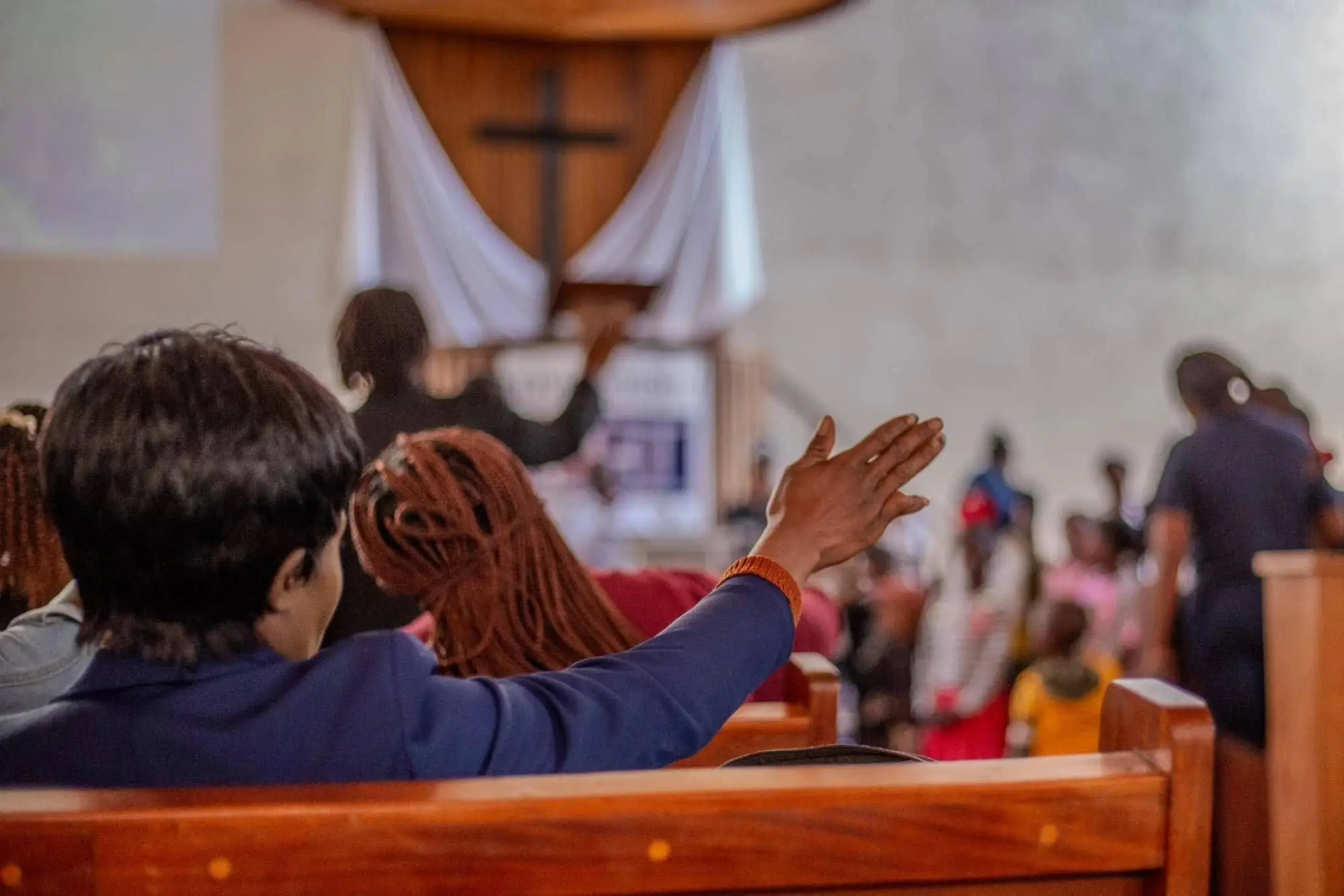 A worshipper raises a hand toward the cross during a Sunday service