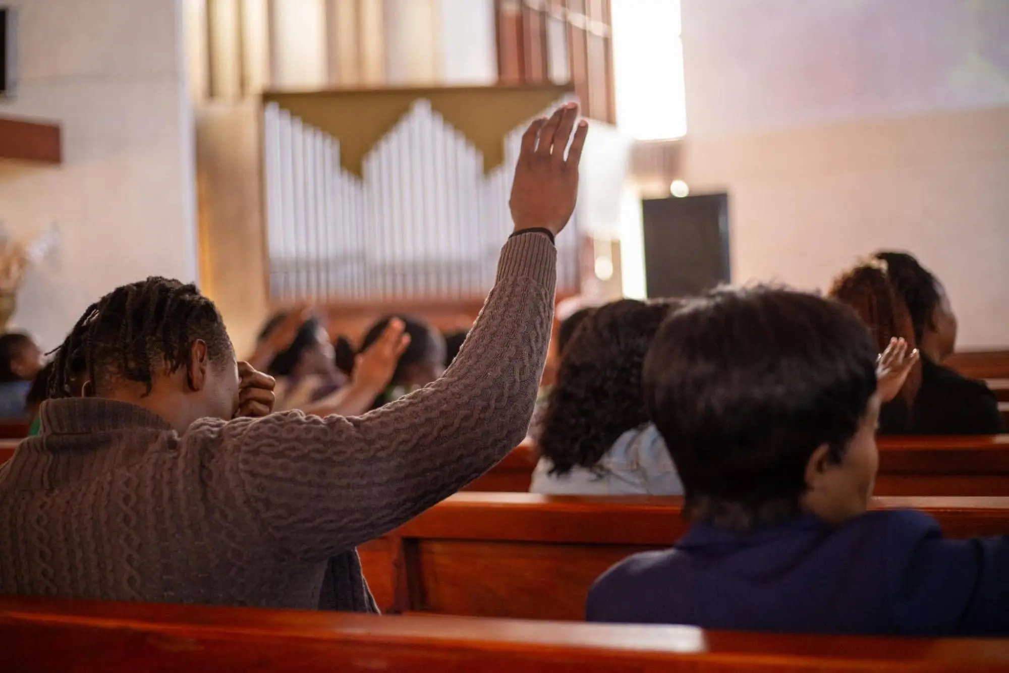 A worshipper raises a hand during praise, with the organ pipes behind